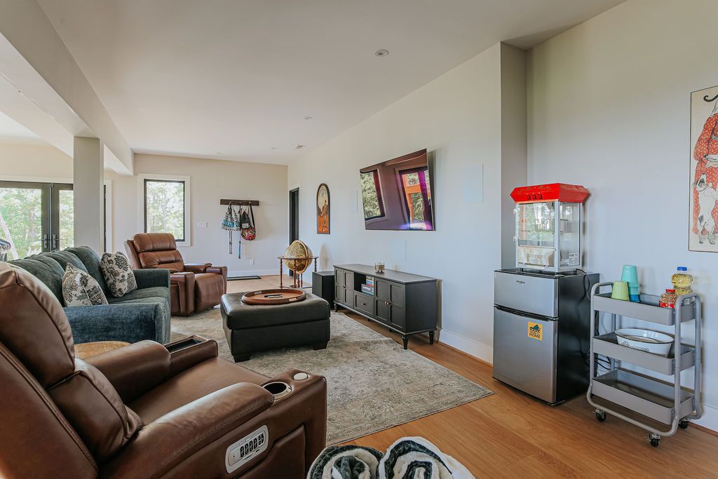 Ein modernes Wohnzimmer mit Sofa, Sessel und Hocker, sowie eine kleine Küchenzeile mit Kühlschrank und ein Wagen mit Geschirr.