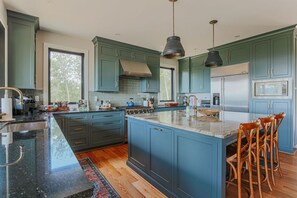 A modern kitchen with teal cabinets, a large island, and a stainless steel refrigerator. - Forever Farm: Private Mtn Estate in Wine Country (Faber)