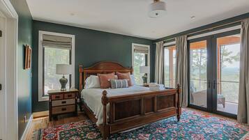 Een slaapkamer met een groot bed, een nachtkastje, een dressoir en uitzicht op de omgeving door een schuifdeur.'