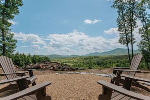 Un espace recouvert de gravier, agrémenté de chaises Adirondack et d’un foyer, offrant une vue sur une chaîne de montagnes boisée.