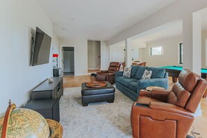 Un salón amplio con mesa de billar, sofás de cuero, un televisor de pantalla plana y un globo terráqueo sobre una mesita.