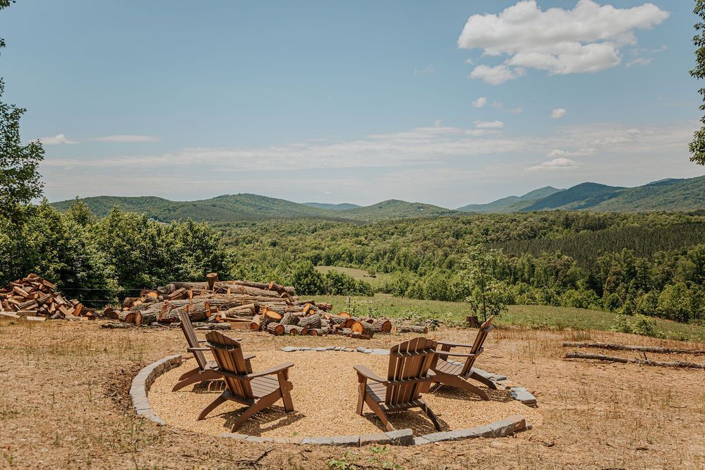 A circular seating area with wooden chairs and a fire pit, surrounded by a natural landscape with hills and trees.