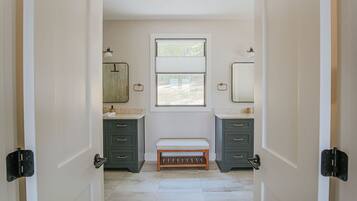 Un bagno con due lavandini, una panca e una finestra.