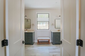 Un baño con dos lavamanos, un banco y una ventana.