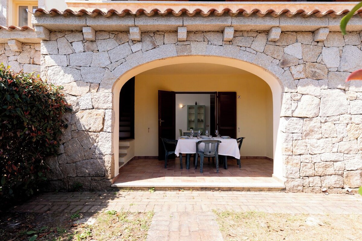 An outdoor dining area with stone walls, a table set for two, and a small archway.