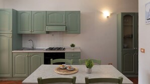 A kitchen with green cabinets, a white countertop, a sink, a stove, and a dining table with chairs.