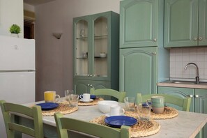 Un coin repas avec une table dressée pour deux personnes, des chaises vertes et une cuisine aux meubles de couleur turquoise.
