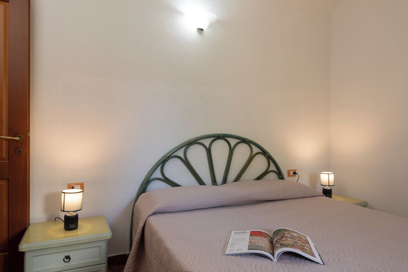 Un lit simple avec une tête de lit, deux lampes de chevet, une table de chevet avec un tiroir et un livre posé sur le lit.