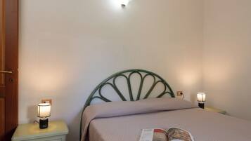Un lit simple avec une tête de lit, deux lampes de chevet, une table de chevet avec un tiroir et un livre posé sur le lit.