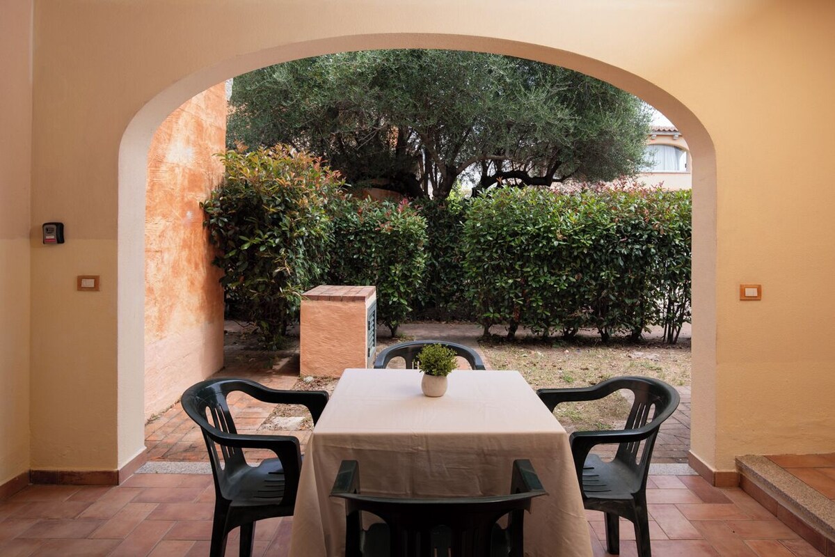 A patio with a table and chairs, an archway, and a view of a garden with trees and bushes.