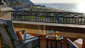 Ein Balkon mit Meerblick, ein Tisch mit Getränken und Snacks sowie ein Stuhl.
