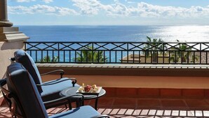 Ein Balkon mit zwei Liegestühlen, einem kleinen Tisch und einer Speiseplatte, mit Blick auf den Ozean.