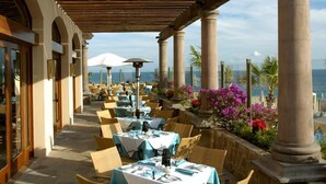 Ein Essbereich im Freien mit Tischen und Stühlen, einer Holzw pergola und Meerblick.