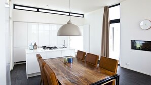 Een moderne keuken met witte kasten, een centraal eiland en een eetgedeelte met een houten tafel en lederen stoelen.