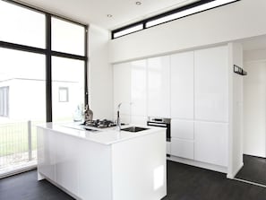 A modern kitchen with a central island, white cabinetry, and a large window providing natural light. - Holiday Home in Breskens With Terrace (Breskens)