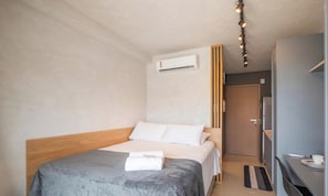 Ein Hotelzimmer mit einem Bett, einem Nachttisch, einem Schreibtisch, einem Stuhl, einer Klimaanlage und einer Tür.