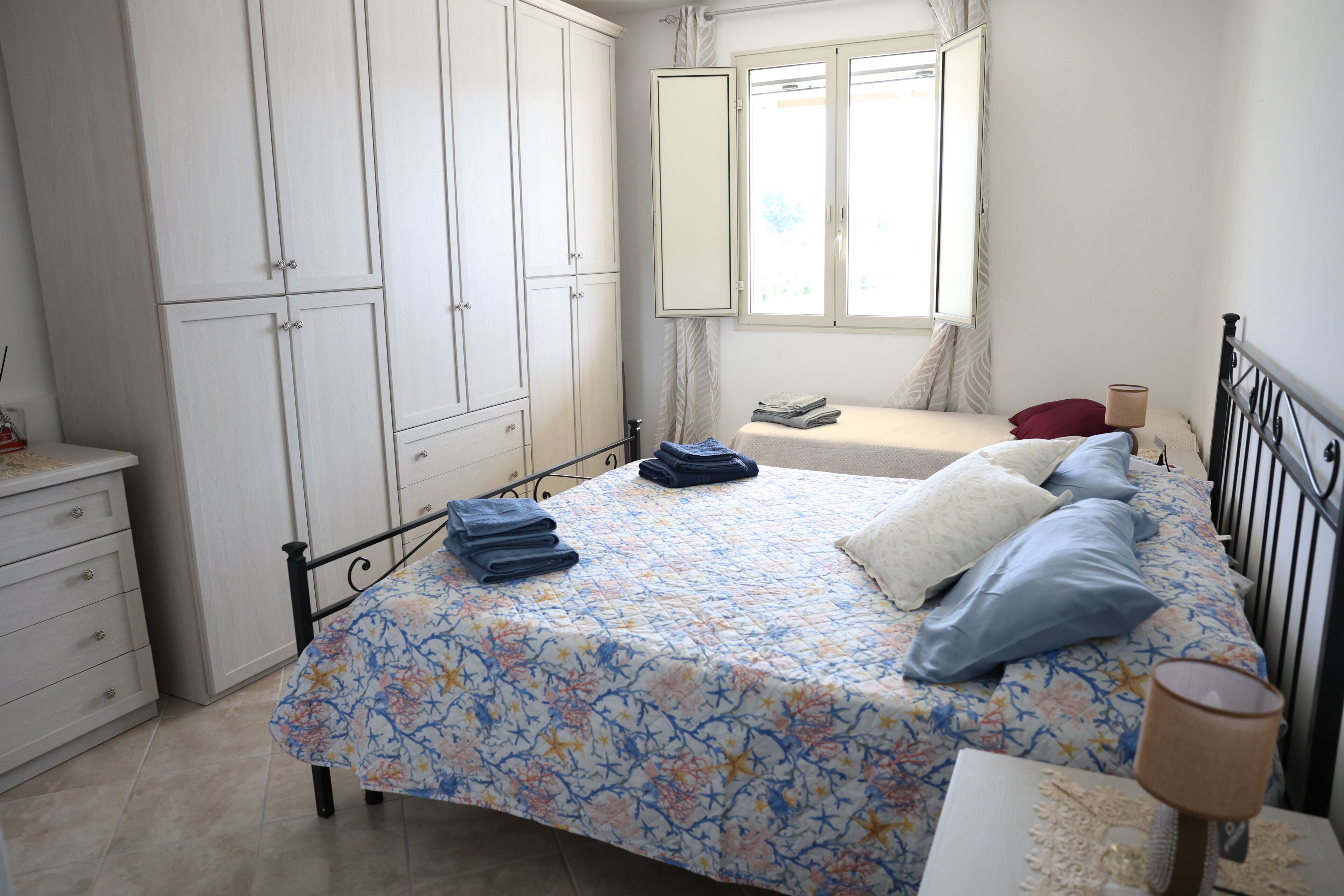 Een slaapkamer met een bed, nachtkastje, dressoir en een raam met gordijnen.