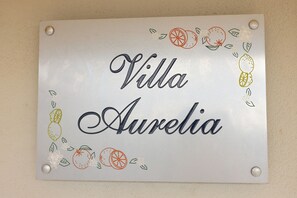 Un letrero con el texto 'Villa Aurelia' rodeado de ilustraciones de frutas.