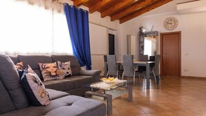 A living room with a sofa, coffee table, and dining area with chairs and a table. - Villa Aurelia | Private Pool, 10 Guests, Near the Sea (Sicilia)