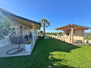 Una casa con un porche cubierto, una zona de barbacoa de piedra y un césped bien cuidado.