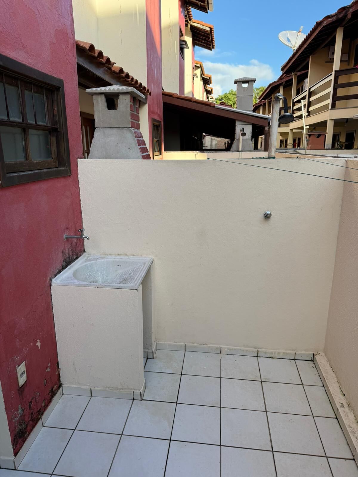 A small, enclosed outdoor area with a tiled floor, a concrete structure, and a satellite dish on a building.