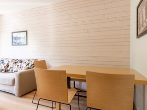 Ein Zimmer mit Holzboden, einem Holztisch mit Stühlen, einer Couch mit gemusterten Kissen und einem gerahmten Bild an der Wand.