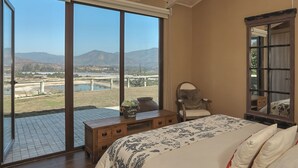 A bedroom with a large bed, a chair, a wooden desk, and a large window offering a view of a landscape. - Villa Fiesole 2-bedroom farmhouse in welcoming Limache perfect for relaxing (Limache)