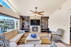 A modern living room with a fireplace, a ceiling fan, and a view of a marina. - VRCC Villa Waterfall (Cape Coral)