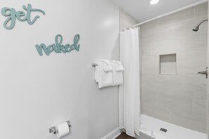 Et badeværelse med bruser, håndklæderække og toiletpapirsholder.