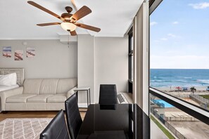 A room with a view of the ocean, a ceiling fan, a sofa, a dining table, and a window. - 🌴Amazing Ocean Views | Beachfront Pool | Oceanside Inn 606🌴 (Daytona Beach)