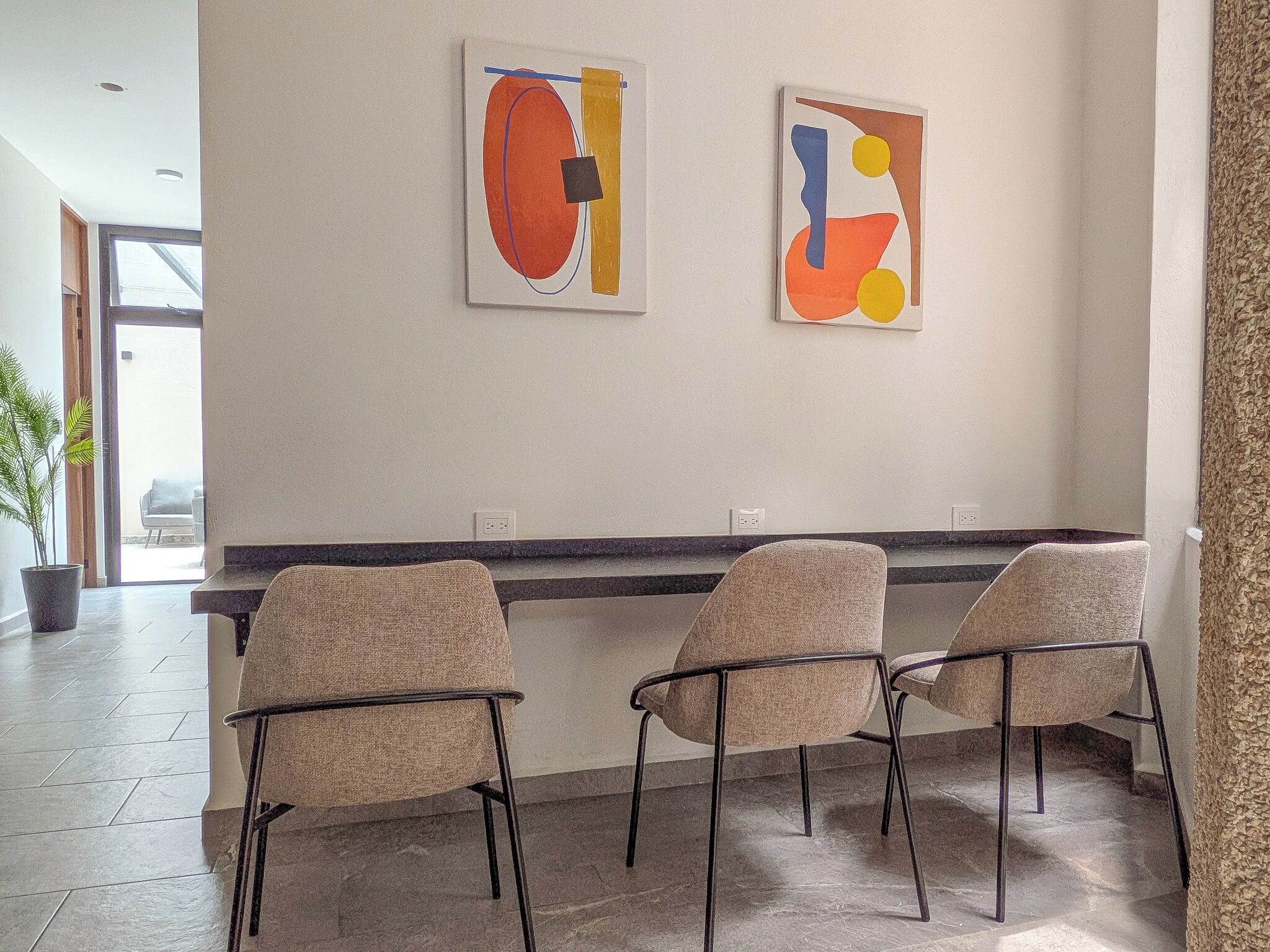 Un intérieur moderne agrémenté de deux œuvres d’art abstrait au mur, d’un coin salon avec trois fauteuils et d’une plante en pot.