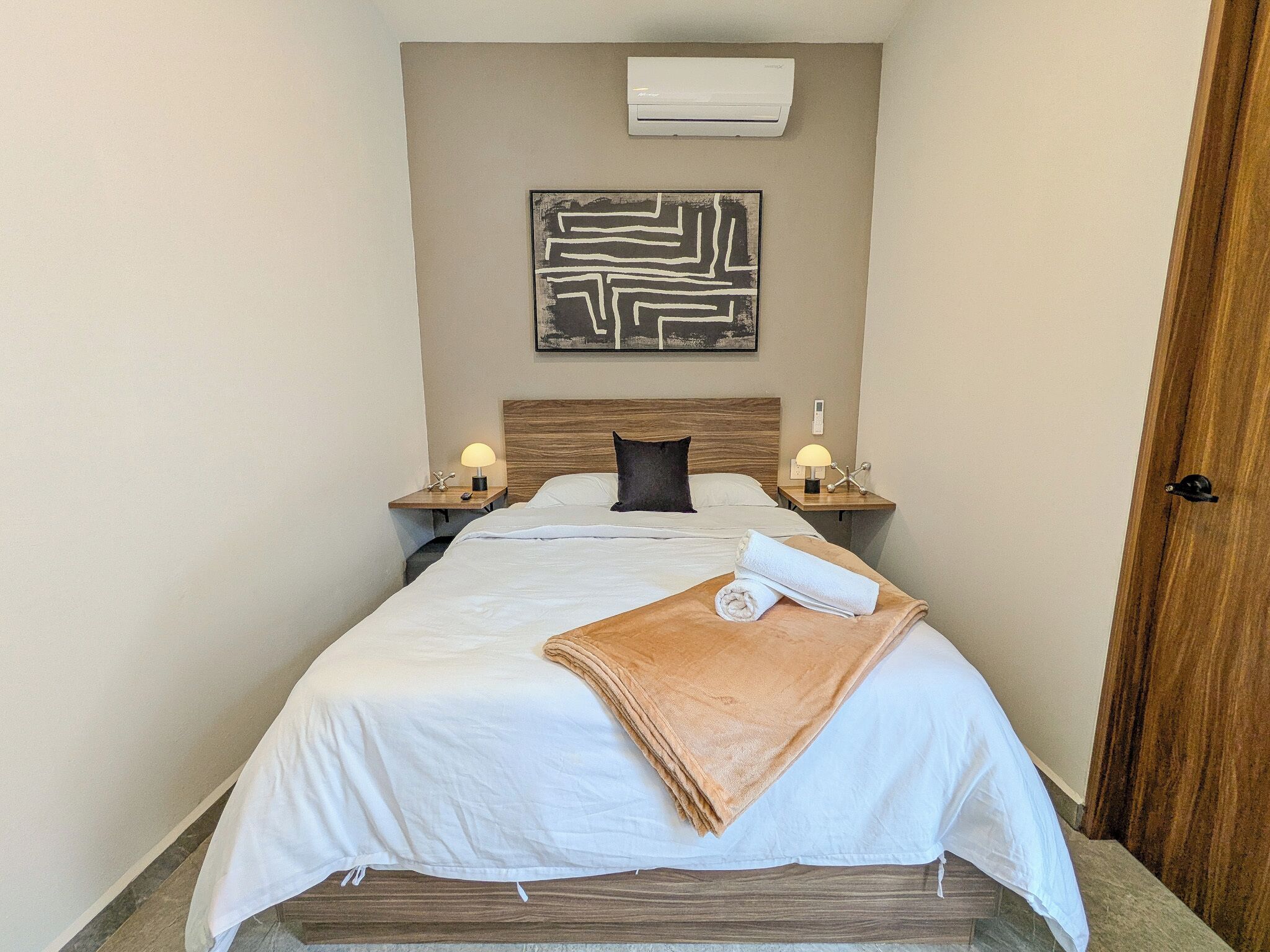 Ein Hotelzimmer mit einem Bett, zwei Nachttischen mit Lampen, einer Wandklimaanlage und einer Tür.