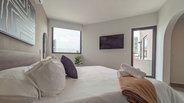 Habitación de hotel con una cama, televisión, ventana y vista a la ciudad.