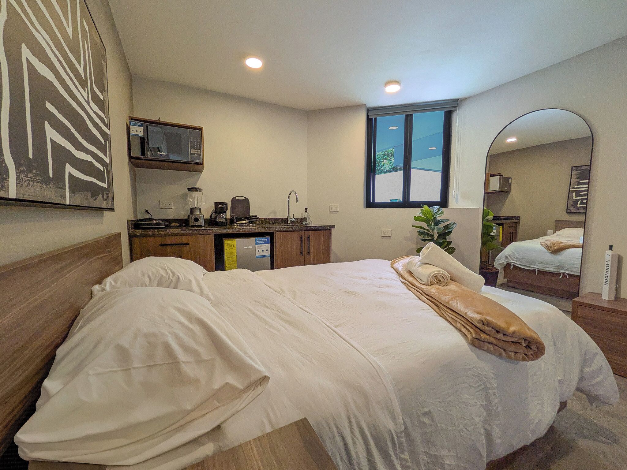 A bedroom with a bed, a bathroom, a kitchenette, and a large window.