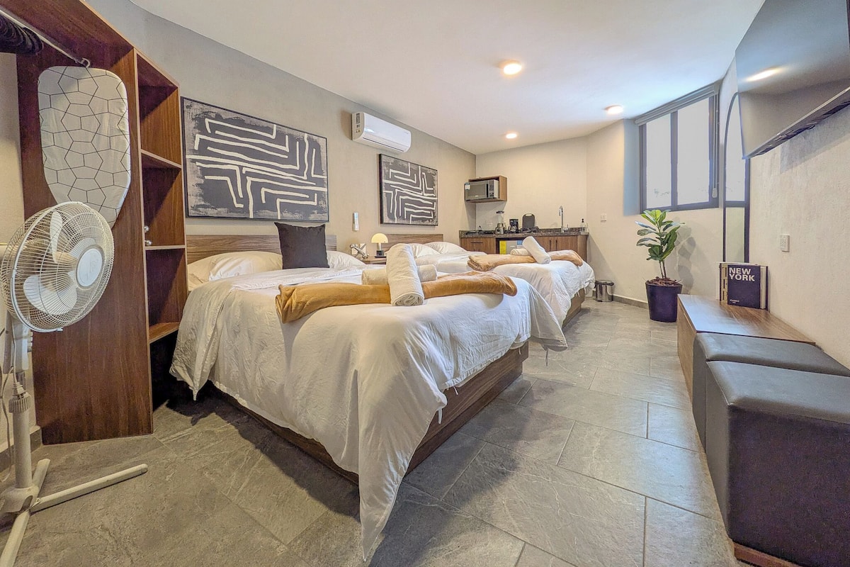 Une chambre d’hôtel avec un lit, un bureau, un ventilateur et une plante en pot.