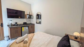 Une chambre d’hôtel comprenant un lit, une petite kitchenette, un miroir et une table de chevet avec une lampe.