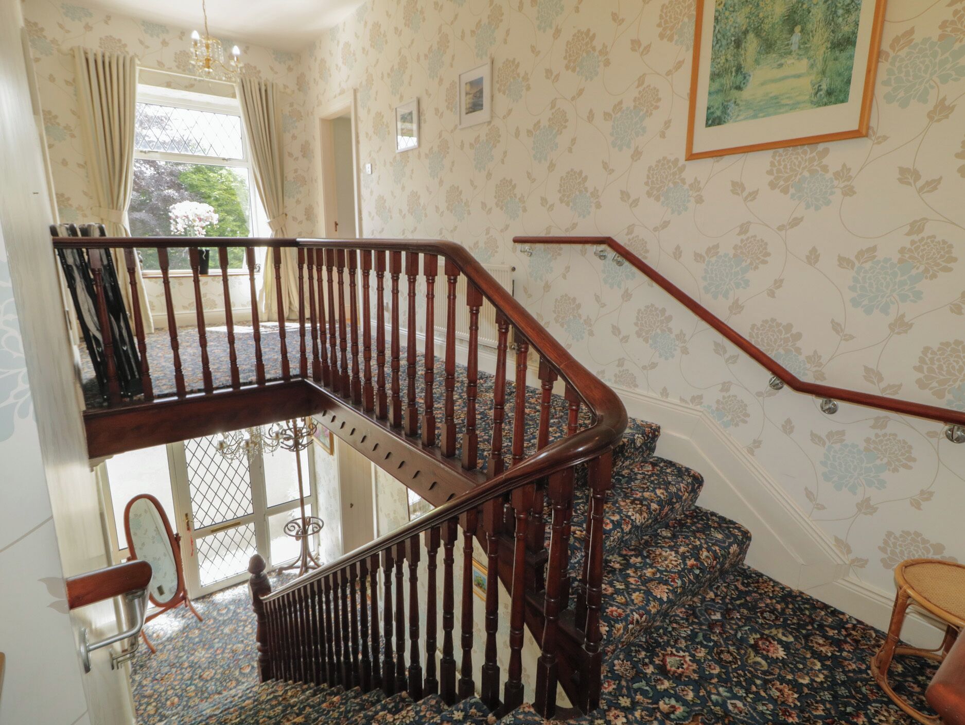 A wooden staircase with a handrail, a patterned carpet, and a door with a mirror.