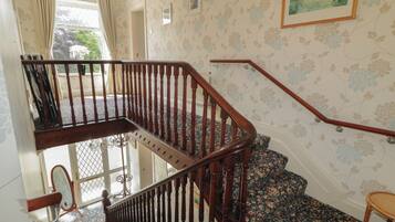 A wooden staircase with a handrail, a patterned carpet, and a door with a mirror.