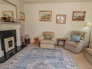A living room with a fireplace, two armchairs, a rug, and framed pictures on the wall.