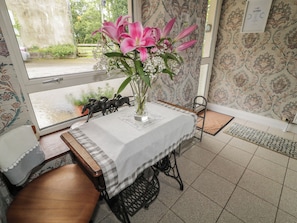 Una habitación con una mesa preparada para dos, un florero con flores, una ventana con vistas y un papel tapiz estampado.
