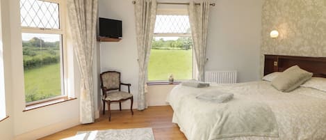 A bedroom with a bed, a chair, a TV, and a view of the outdoors.