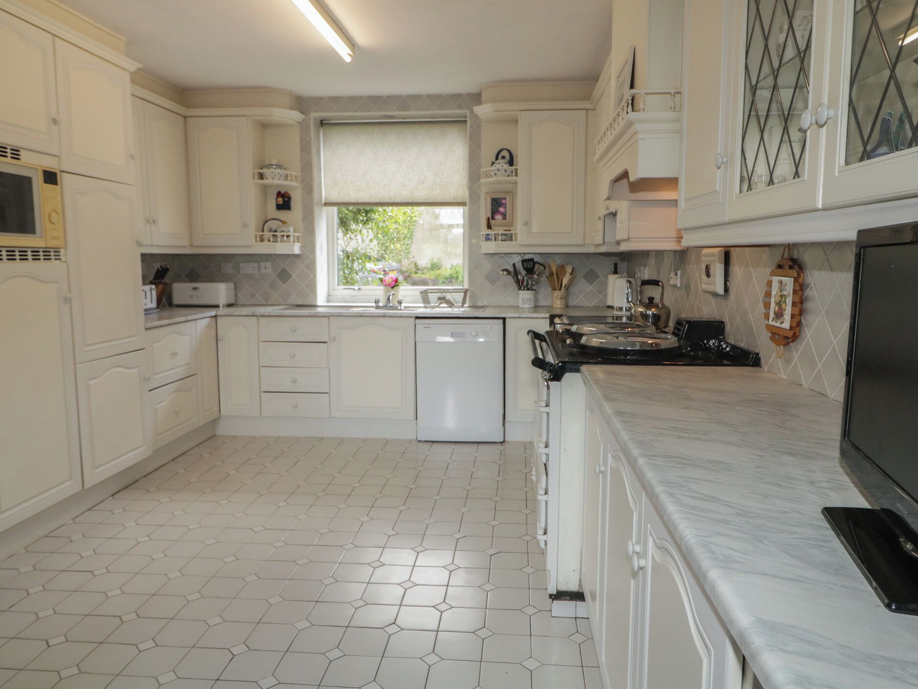 A kitchen with white cabinets, a dishwasher, a stove, and a window with a view of greenery.