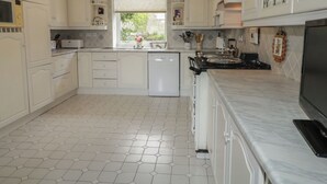 Une cuisine avec des meubles blancs, un lave-vaisselle, une cuisinière et une fenêtre donnant sur un paysage verdoyant.