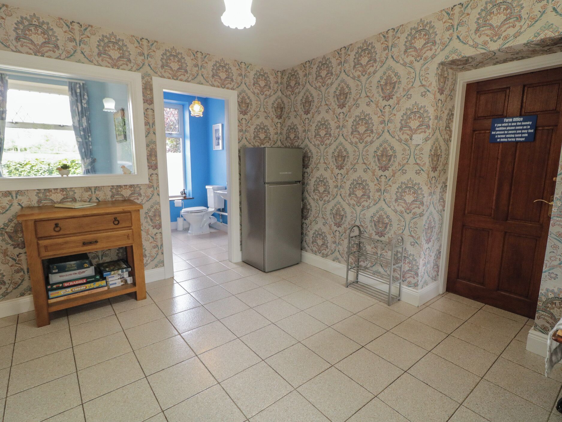 A room with a wooden cabinet, a refrigerator, a door with a sign, and a window with curtains.