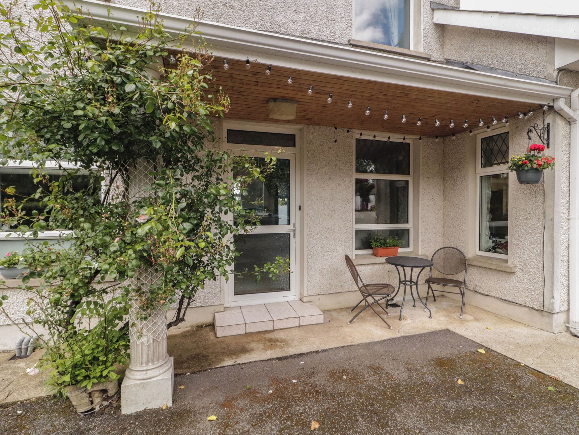 A covered patio with a table and chairs, a potted plant, and a hanging flower basket.