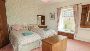 Une chambre avec deux lits, une armoire en bois, une fenêtre avec des rideaux et un miroir.