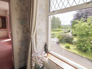 A room with a window overlooking a garden, a curtain, and a vase with flowers.