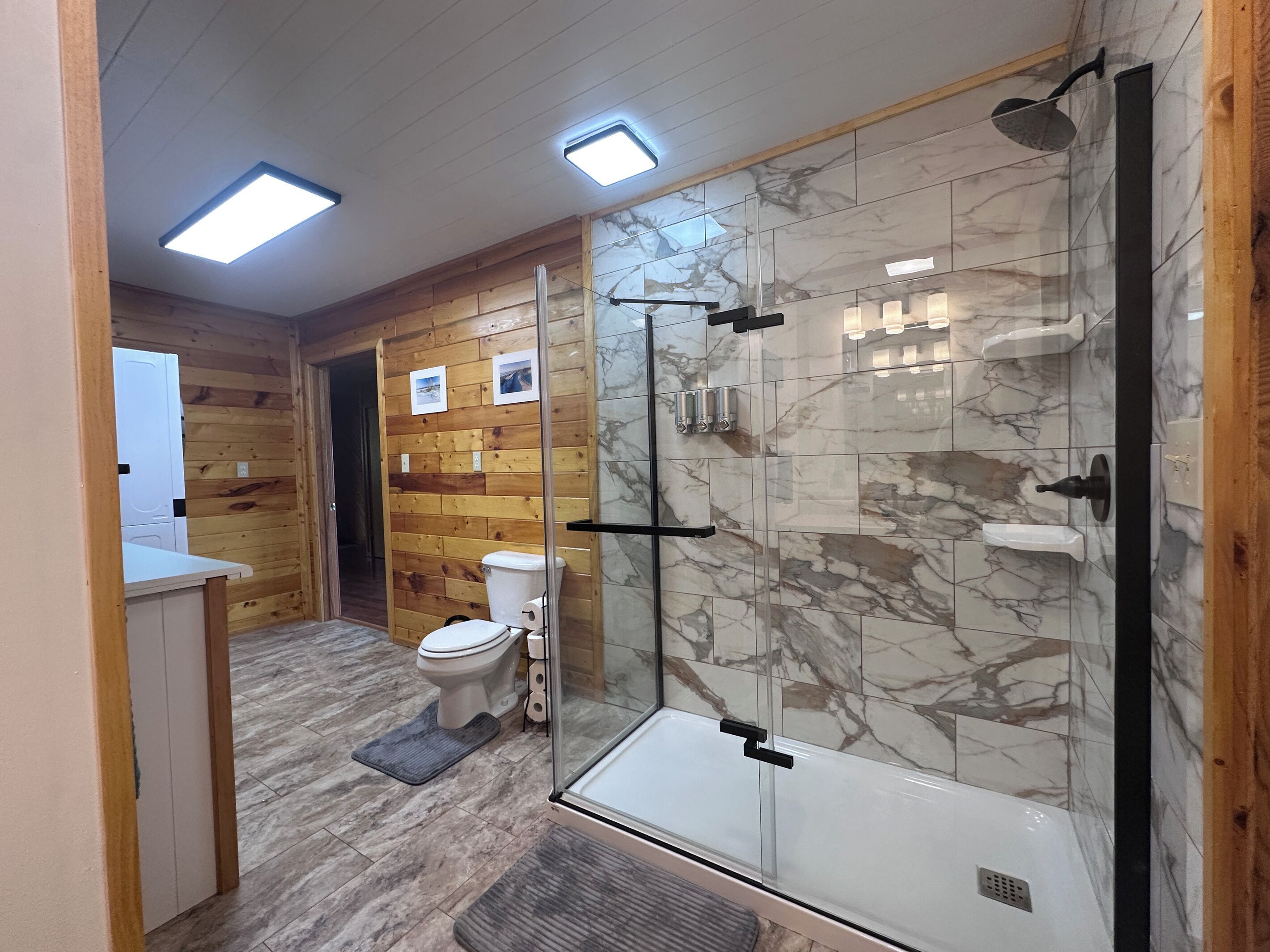 A modern bathroom with a glass shower enclosure, a toilet, and wooden paneling.