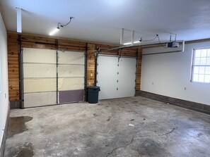 A garage with two large doors, a concrete floor, wooden paneling on the walls, and a ceiling-mounted projector.