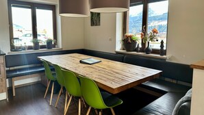 A dining area with a wooden table, green chairs, and pendant lights. - Chalet With Mountain View (Piesendorf)